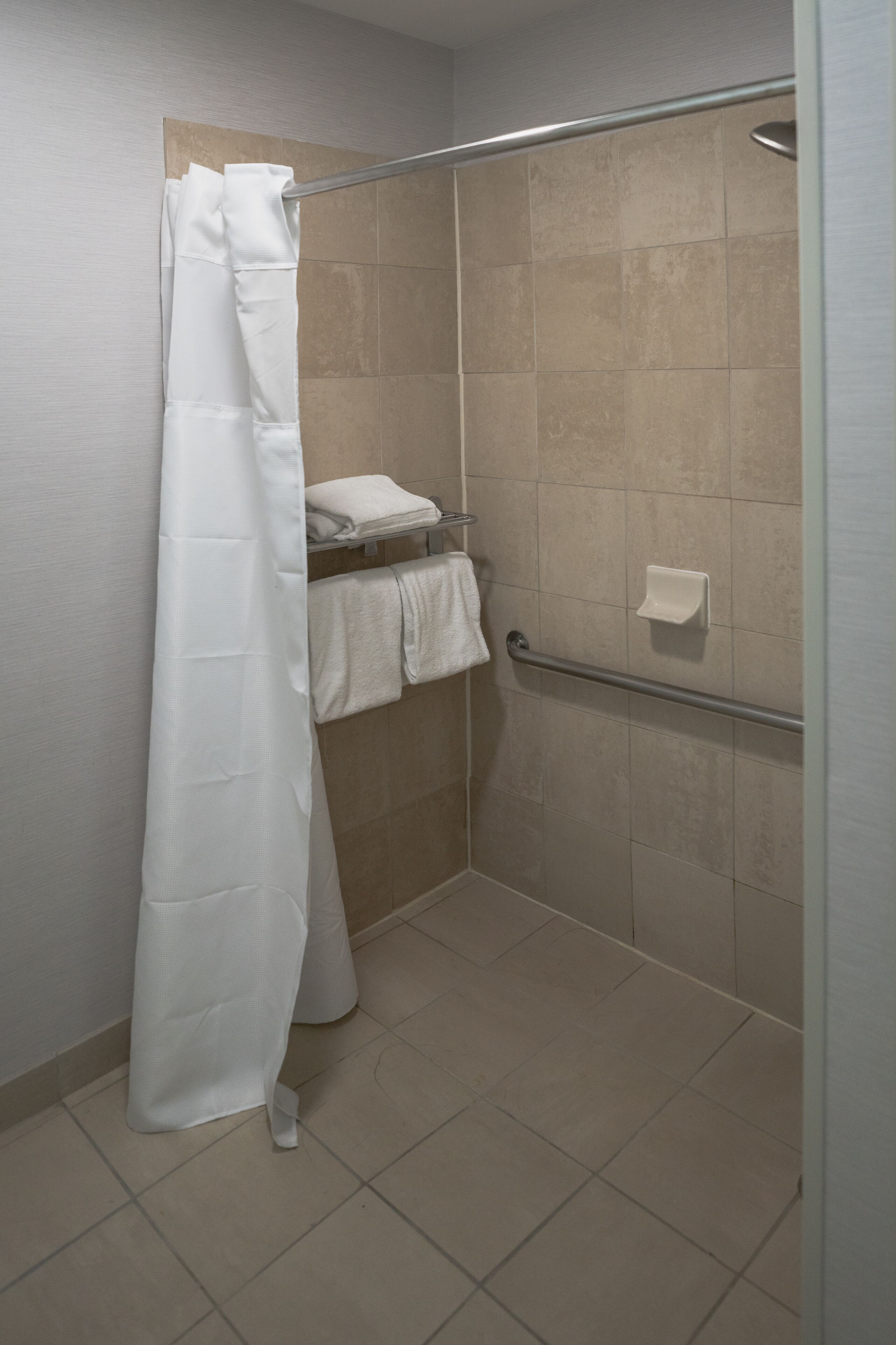 A shower area with a white shower curtain, a towel rack with folded towels, and a grab bar.