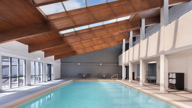 An indoor swimming pool with clear water, wooden ceiling beams, and large windows.