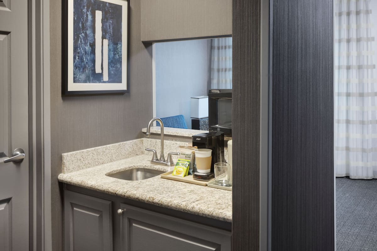 A hotel bathroom with a sink, mirror, and coffee maker.
