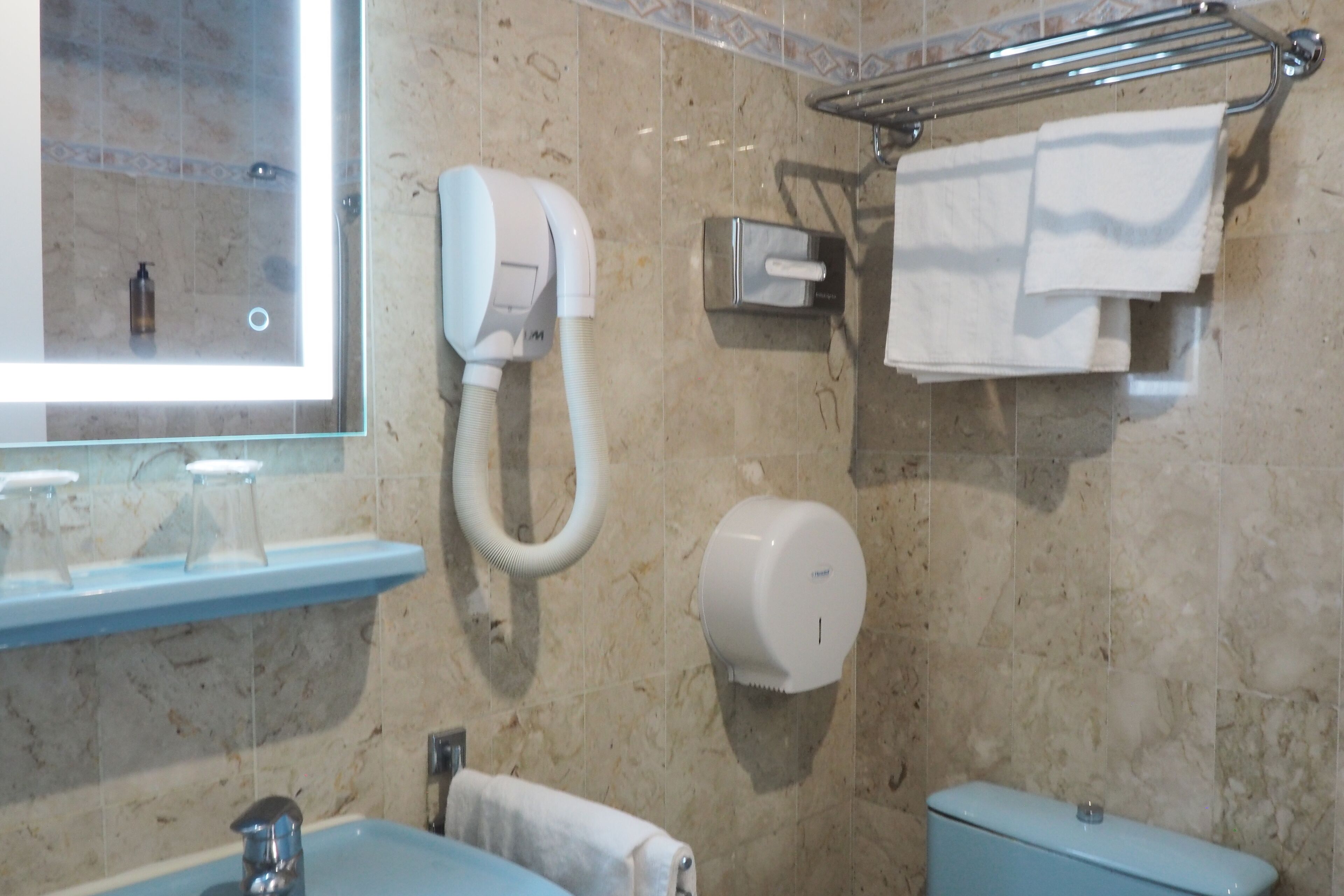 Un baño con lavamanos, espejo, toallero, secador de manos e inodoro.