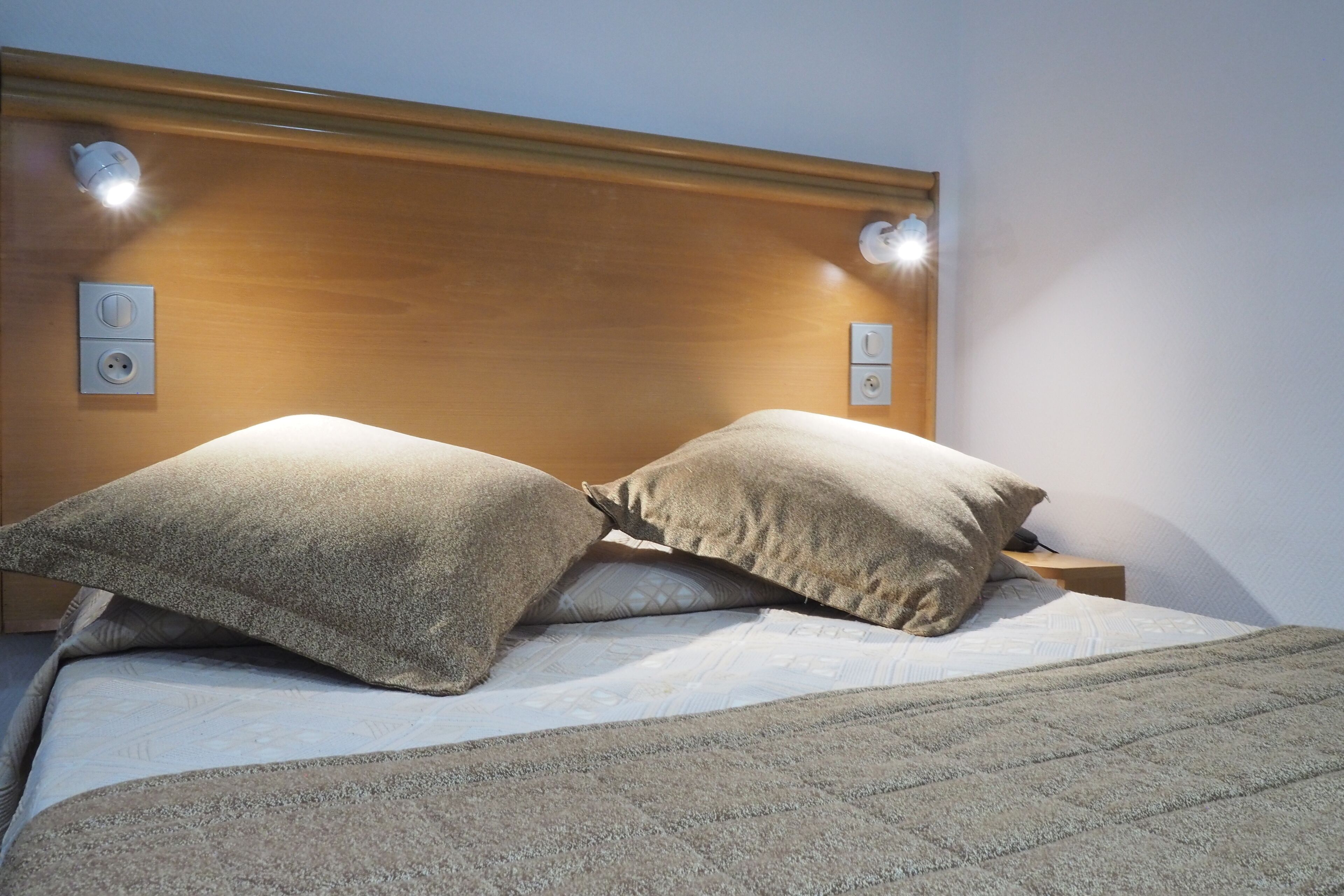 A bed with a wooden headboard, two pillows, and a blanket.