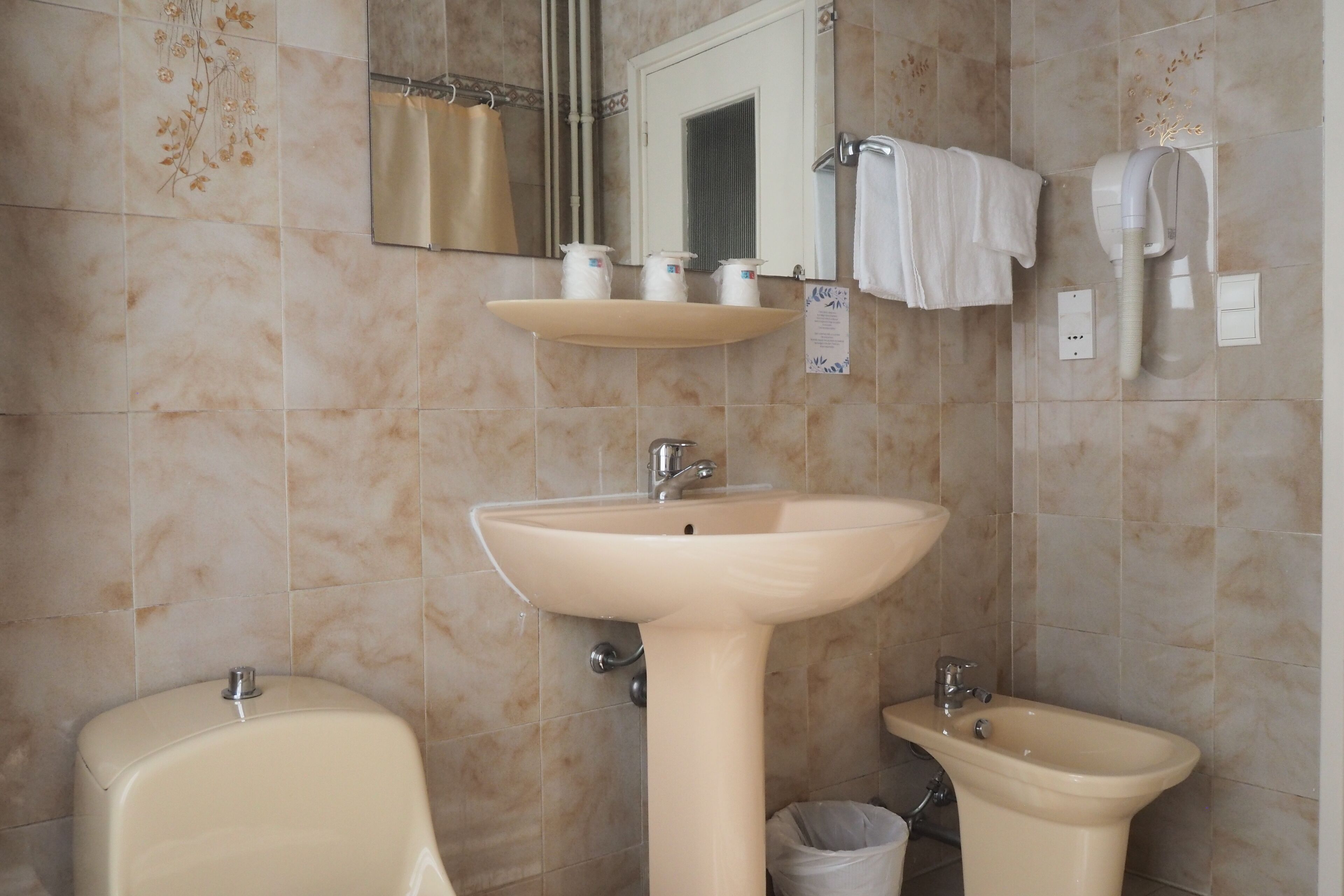 Une salle de bain avec un lavabo beige, des toilettes et un bidet. Deux distributeurs de savon sont placés sur une étagère au-dessus du lavabo.