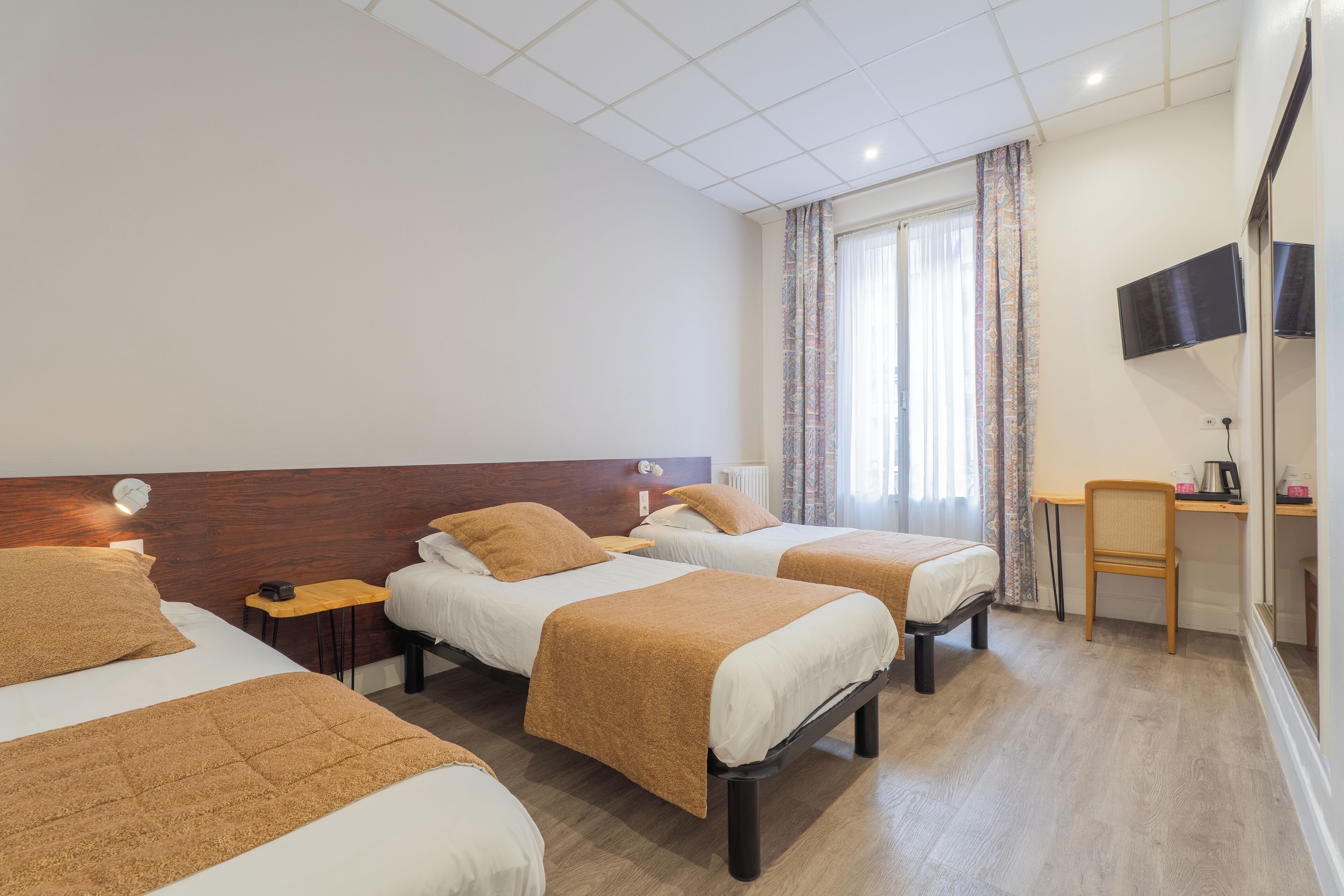 A hotel room with three beds, a desk, a chair, and a TV.