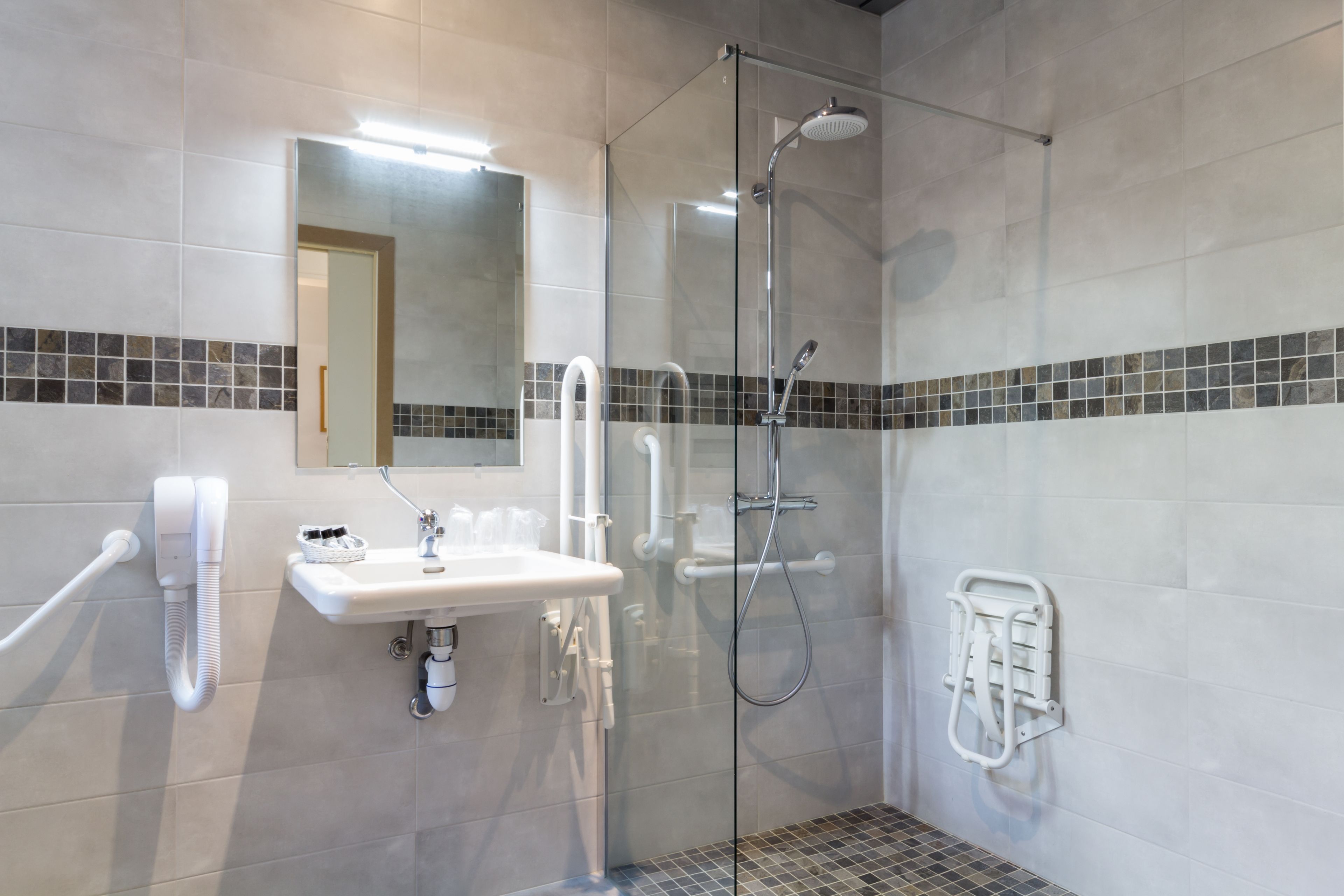 Une salle de bain moderne avec une douche à l’italienne en verre, un lavabo blanc avec un miroir au-dessus et un porte-serviettes fixé au mur.