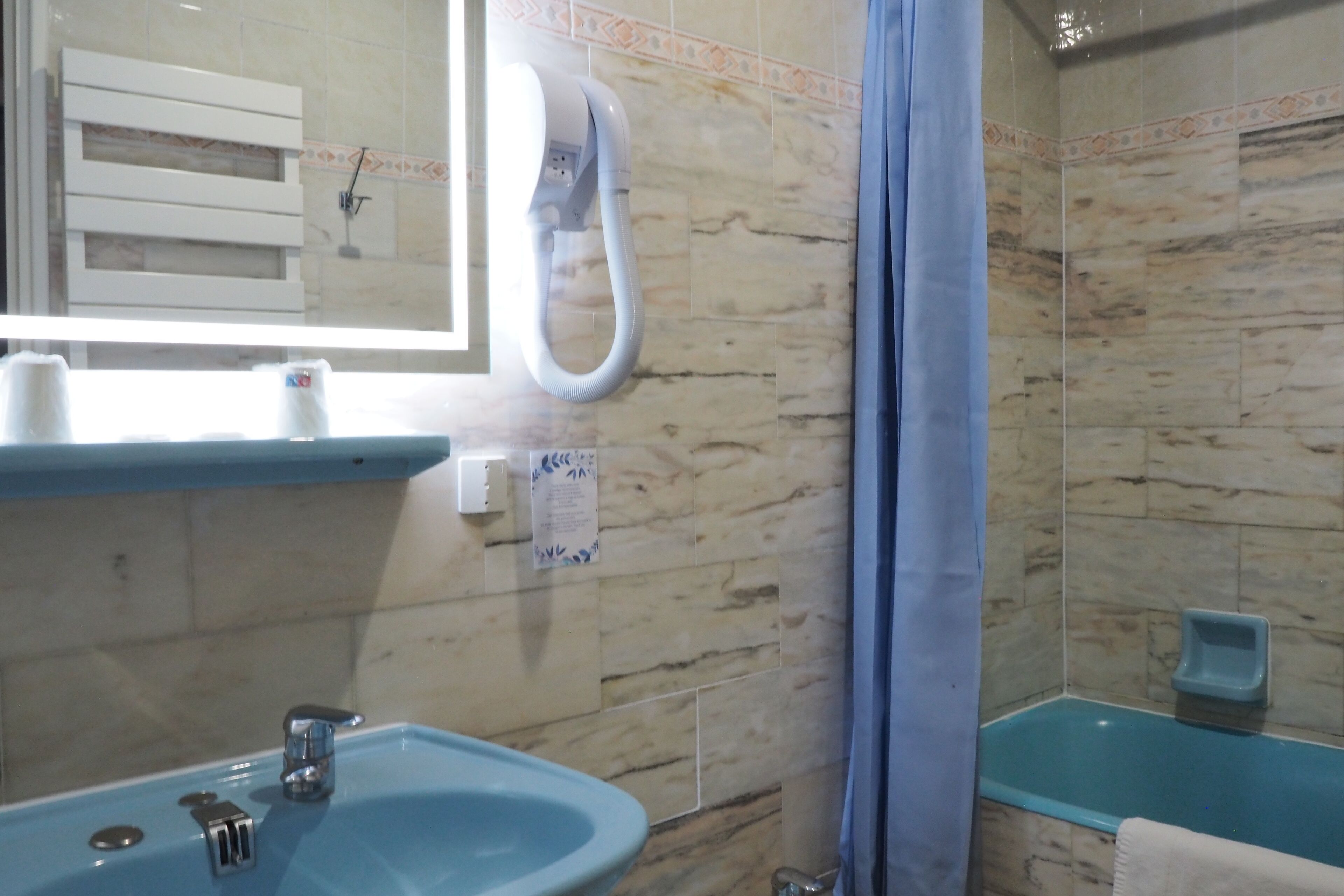 A bathroom with a sink, mirror, towel rack, shower, and a blue bathtub.