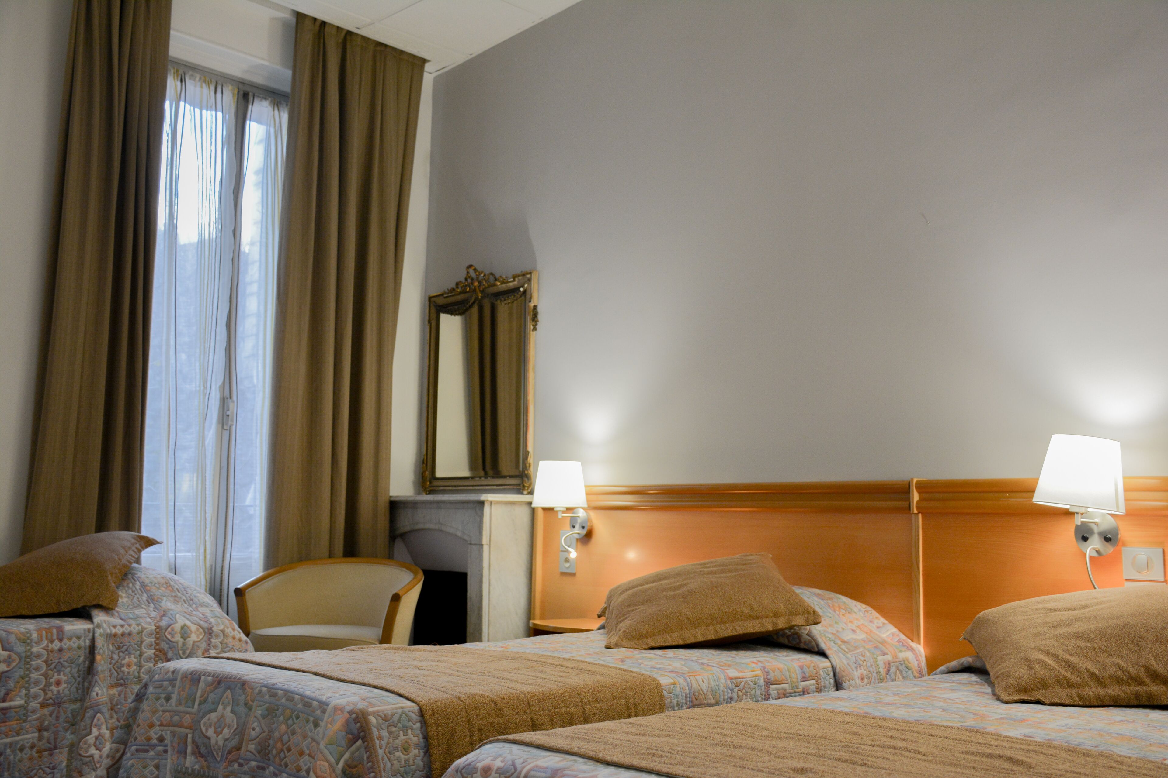 Une chambre d’hôtel avec deux lits, une tête de lit en bois, un miroir et une chaise.