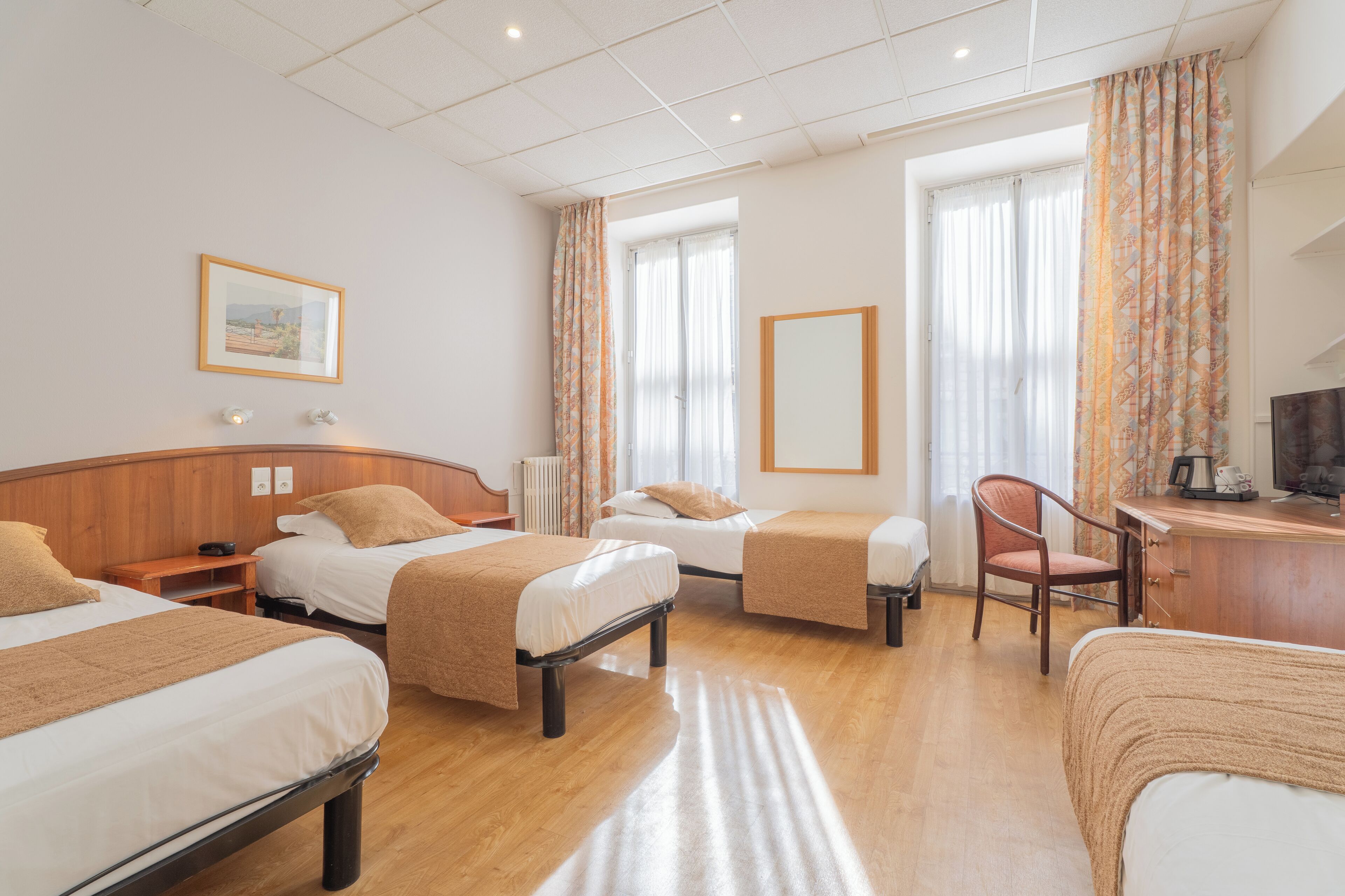 A hotel room with three beds, a desk, a chair, and a large window with curtains.