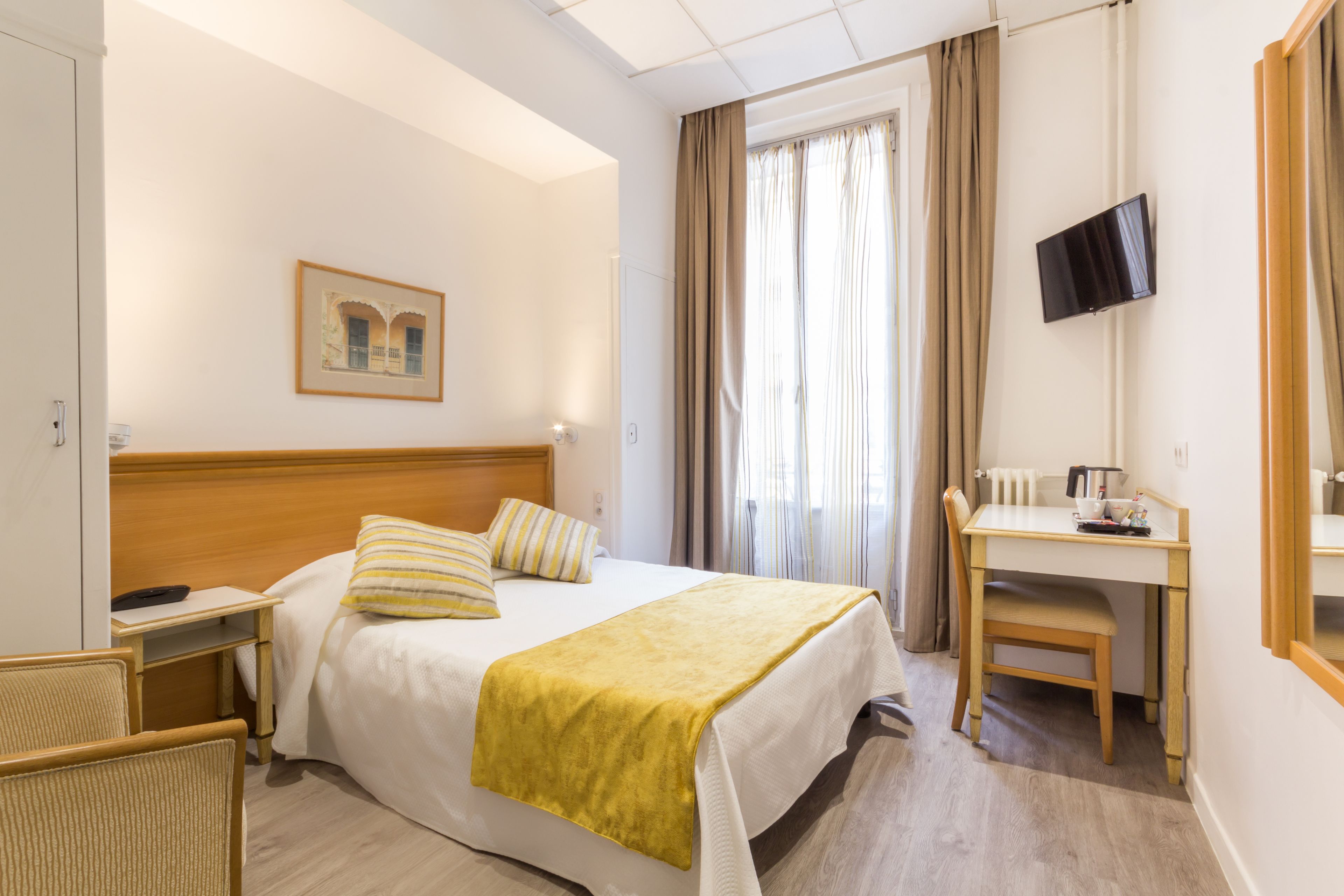 Habitación de hotel con cama, mesita de noche, silla, escritorio y televisor.