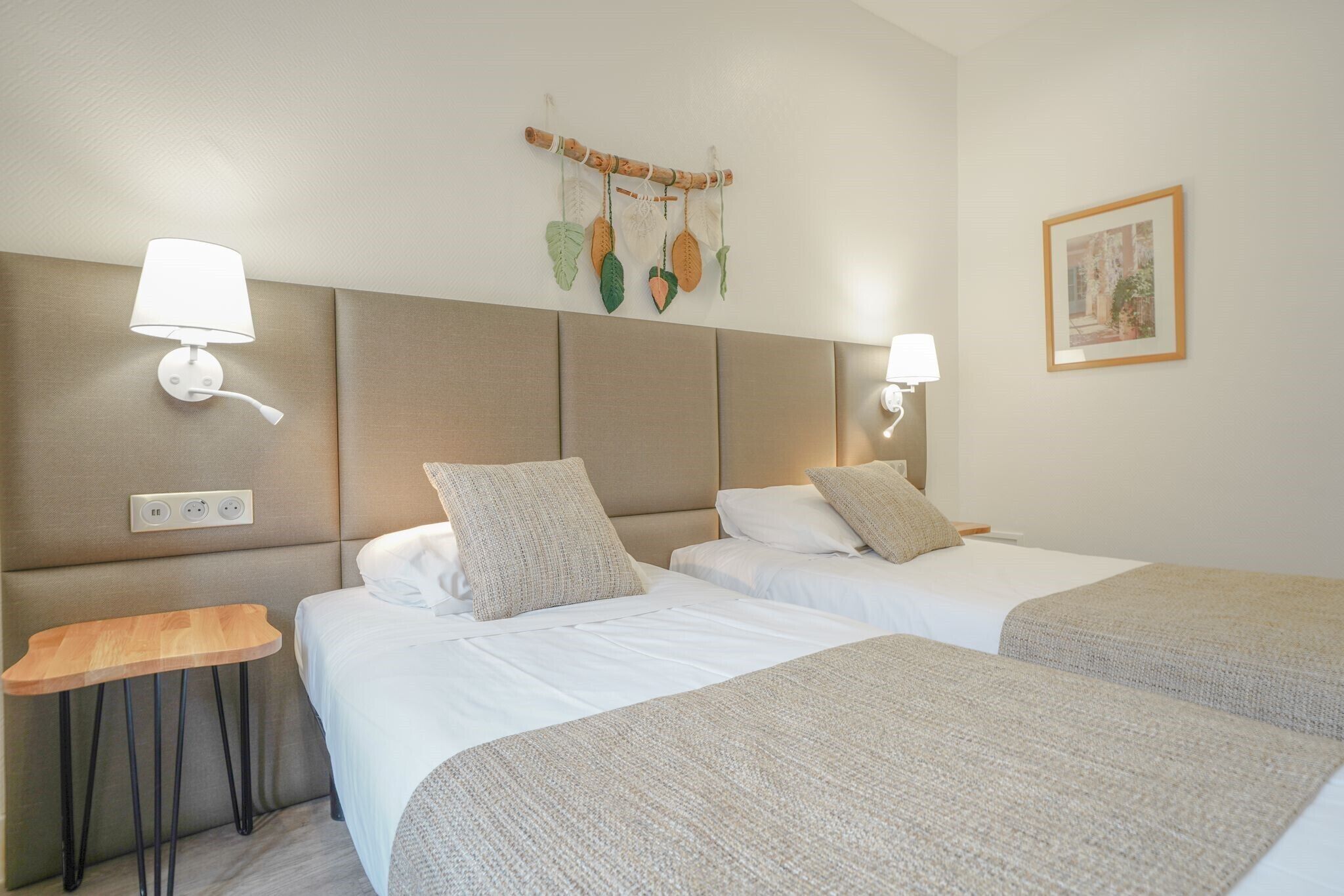 Habitación de hotel con dos camas, una mesita de noche, lámparas fijadas a la pared y un adorno colgante.