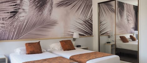 Ett hotellrum med två sängar, en stor spegel och en vägg med ett mönster av palmblad.