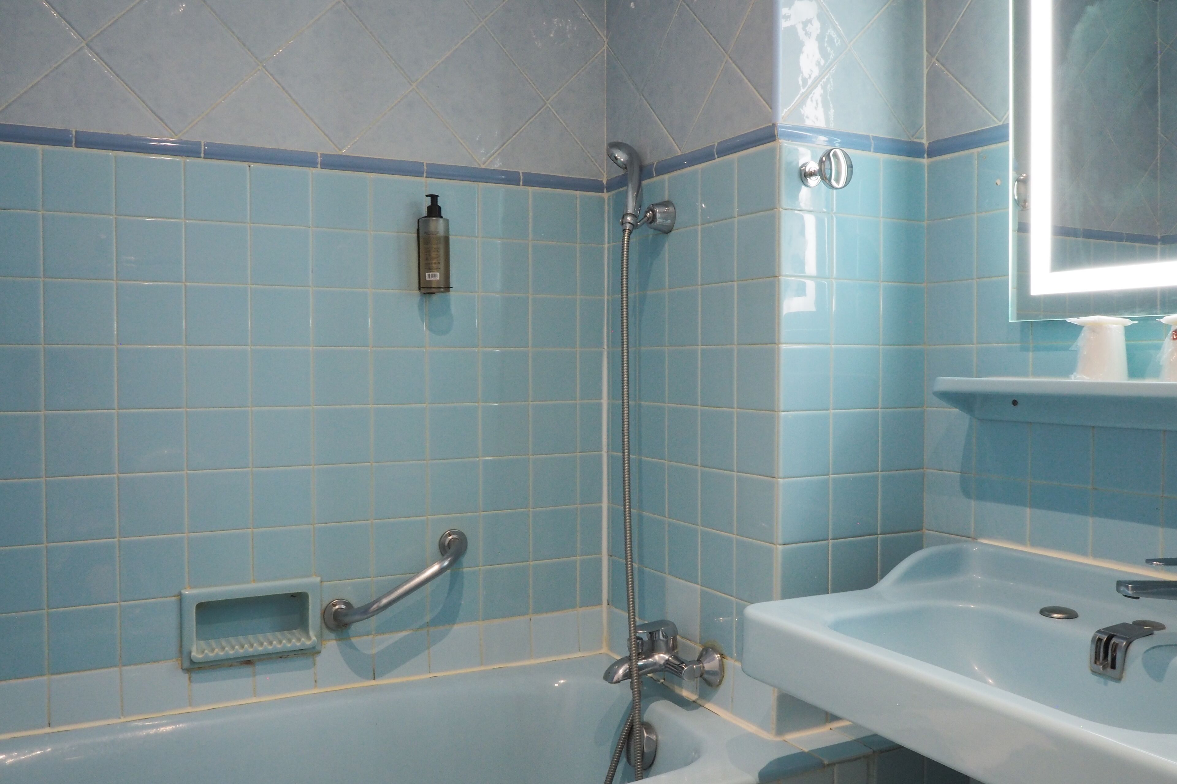 Ein Badezimmer mit blauen Fliesen, einer Badewanne, einer Dusche, einem Waschbecken und einem Spiegel.