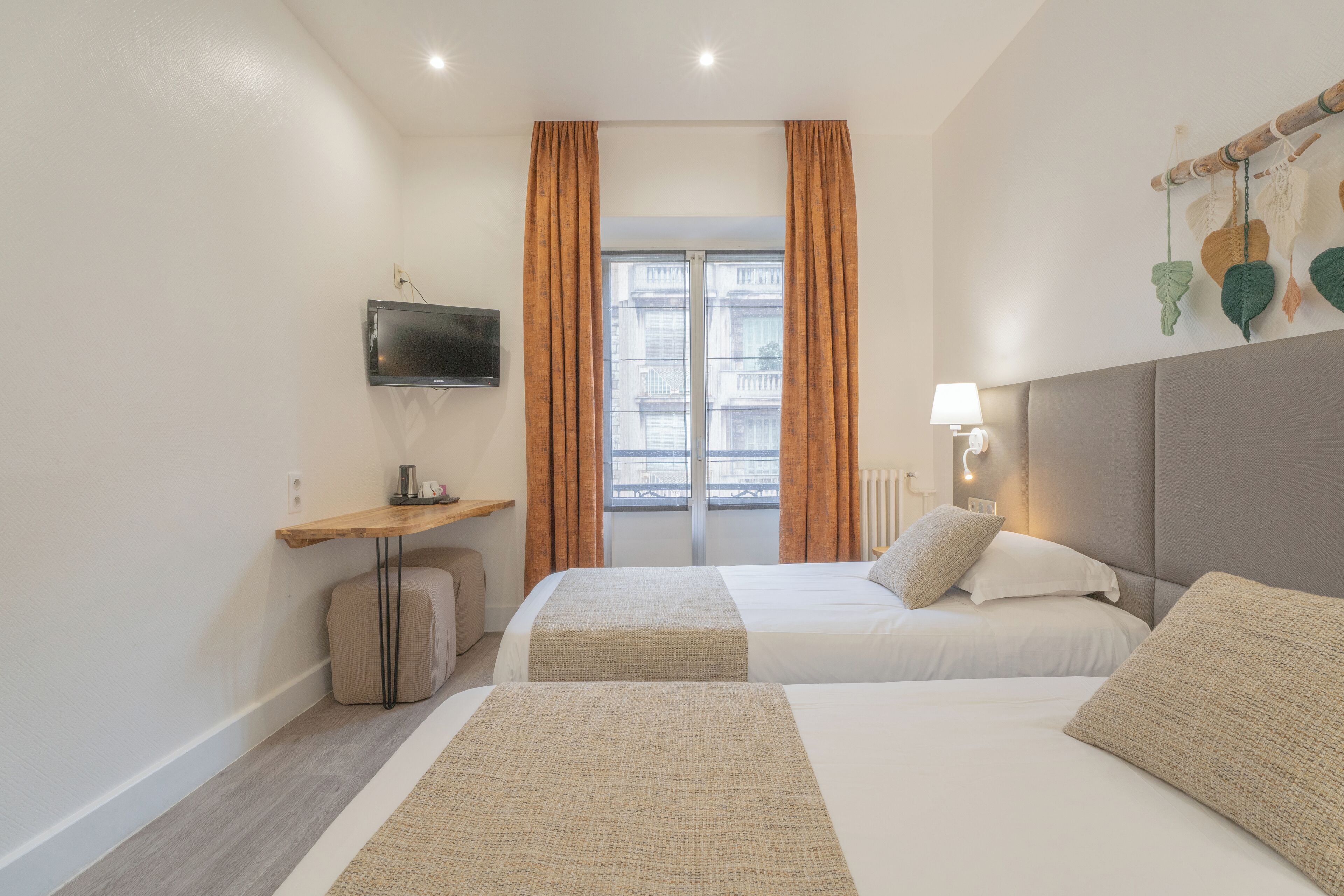 A hotel room with two beds, a TV, a desk, and a window with curtains.