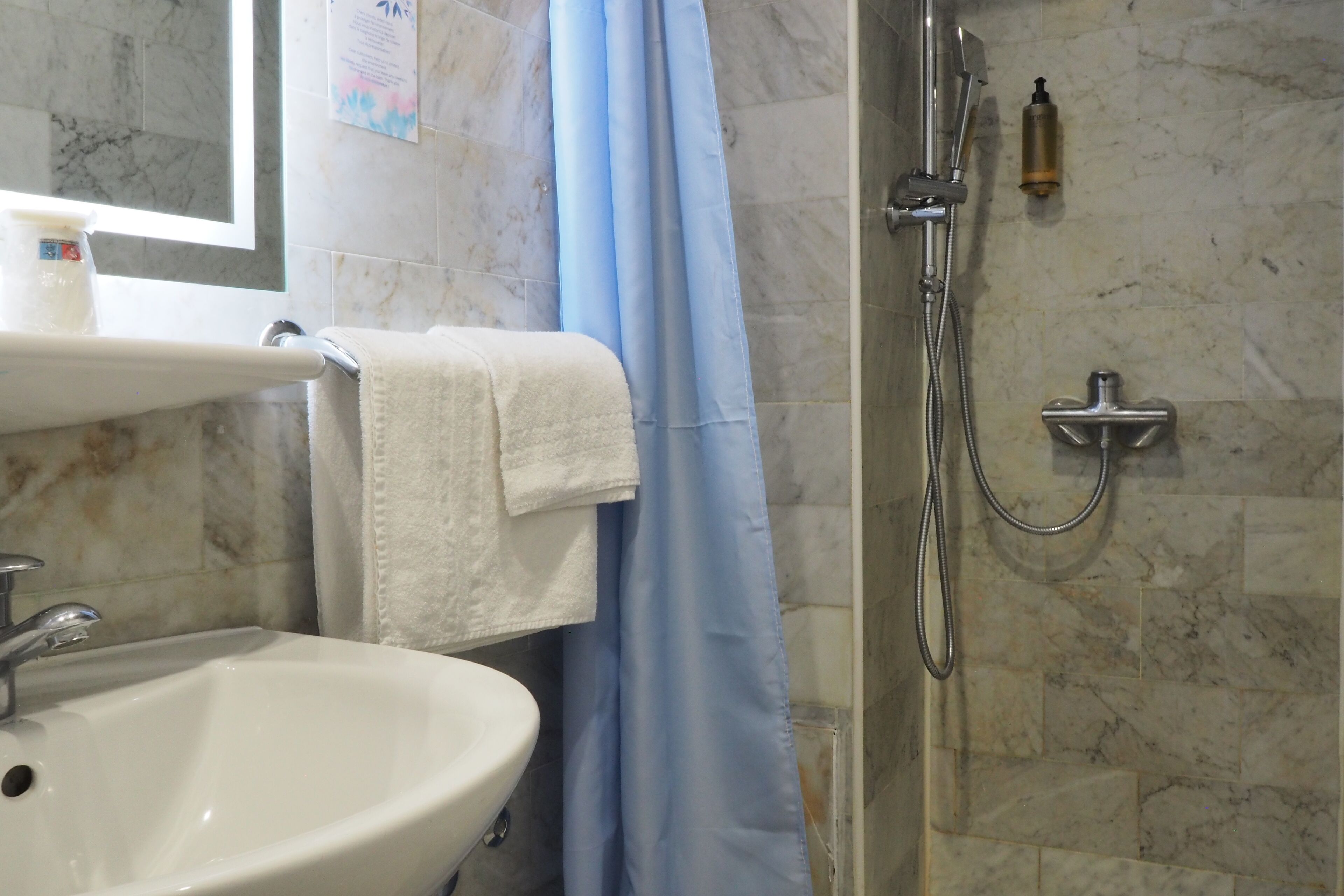 A bathroom with a sink, a mirror, a shower with a handheld showerhead, and a towel hanging on a rack.