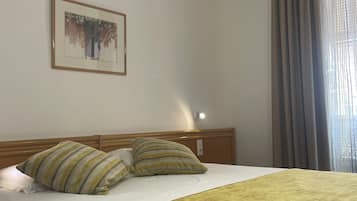 A hotel room with a bed, two pillows, a blanket, a framed picture on the wall, and a window with curtains.