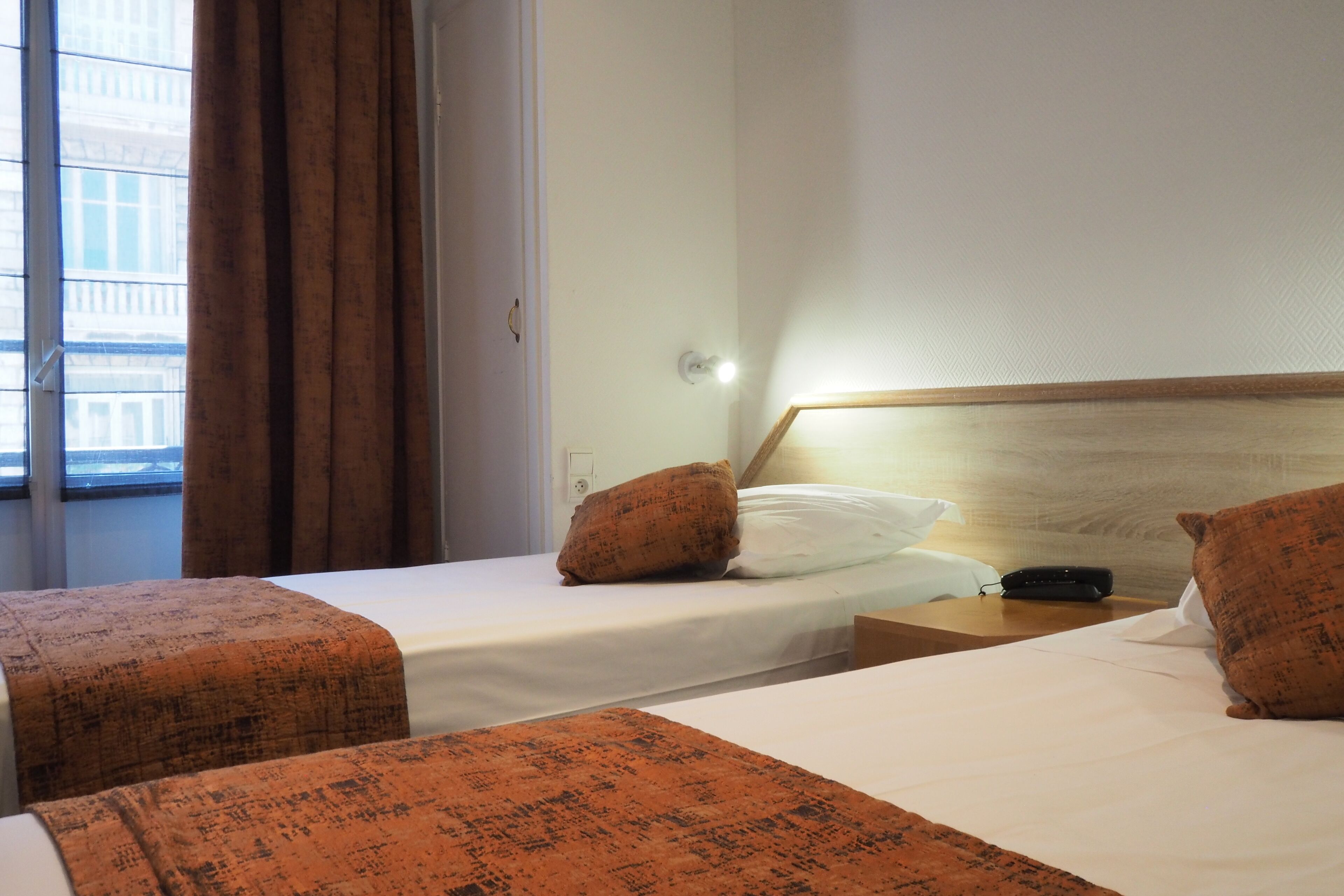 Een hotelkamer met twee bedden, een houten hoofdbord, een nachtkastje en een raam met gordijnen.