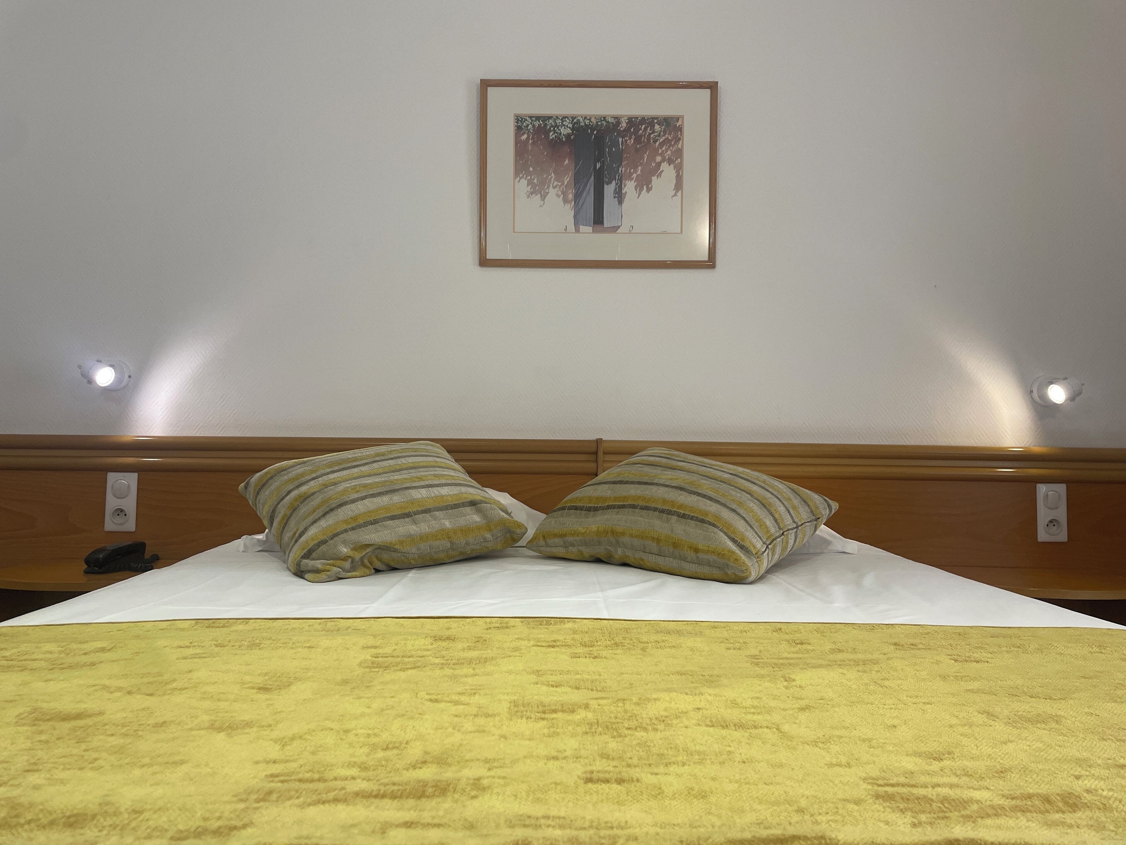 A neatly made bed with two striped pillows, a framed picture on the wall, and a yellow blanket.