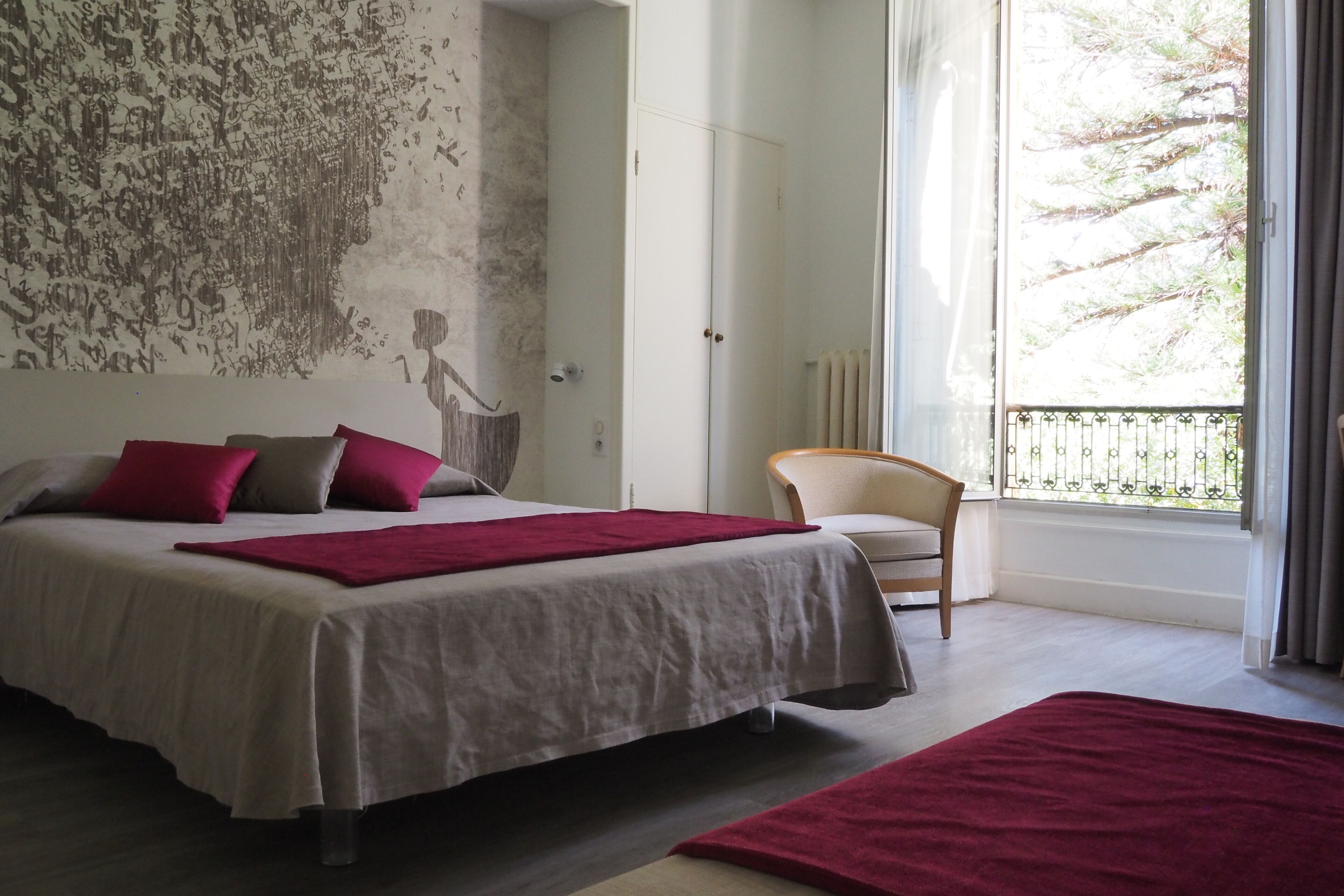 Un dormitorio con una cama grande, una silla y vistas a los árboles a través de una ventana.