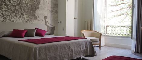 Un dormitorio con una cama grande, una silla y vistas a los árboles a través de una ventana.
