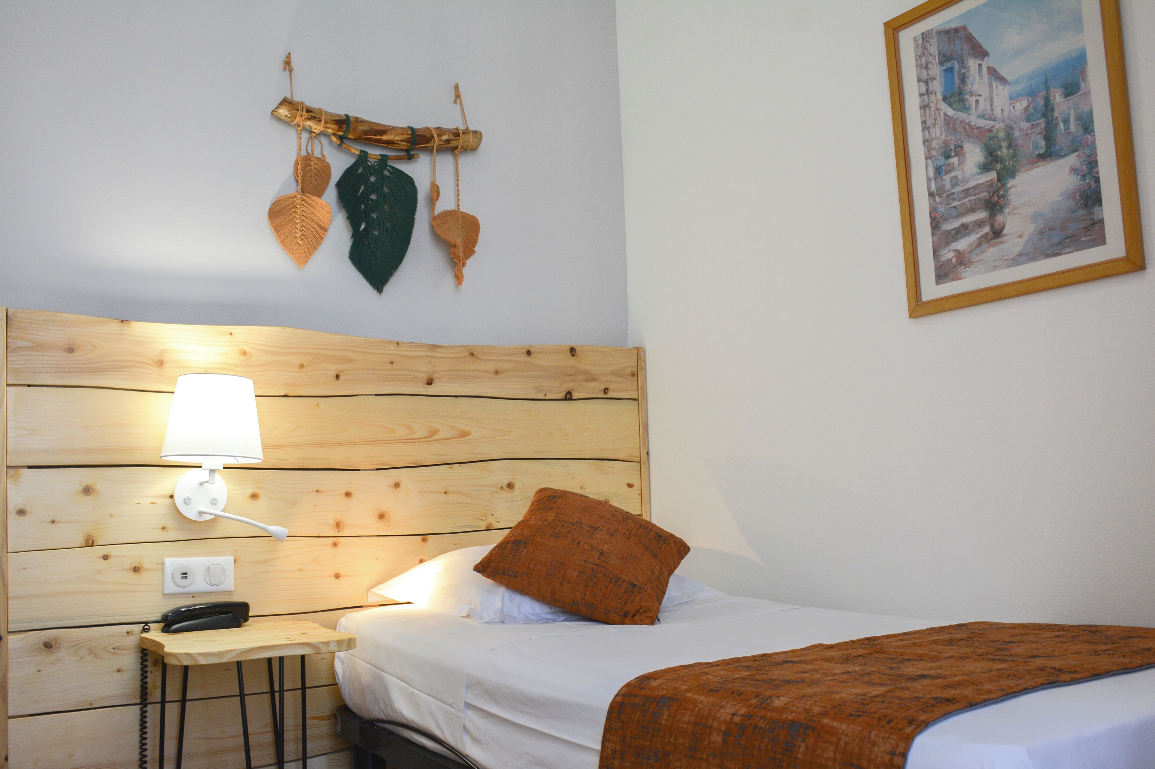 A neatly made bed with a wooden headboard, a bedside table with a lamp, and a wall-mounted plant.