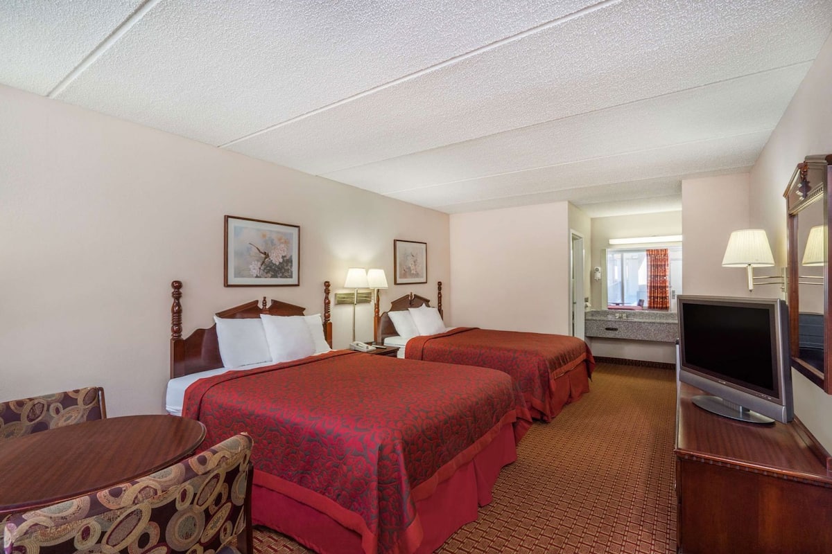 A hotel room with two beds, a TV, a desk, and a chair.