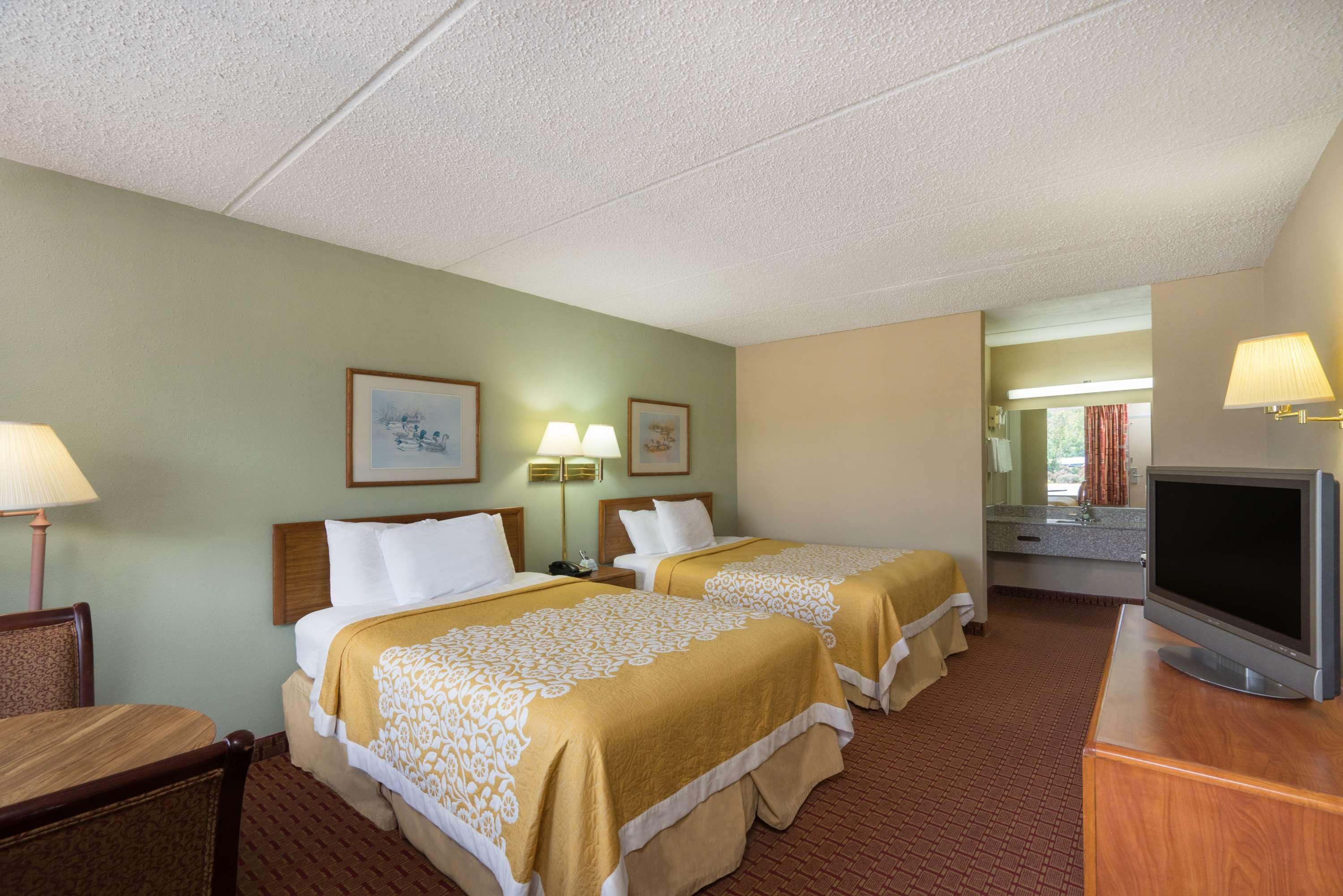 A hotel room with two beds, a television, a desk, and a bathroom visible through an open door.