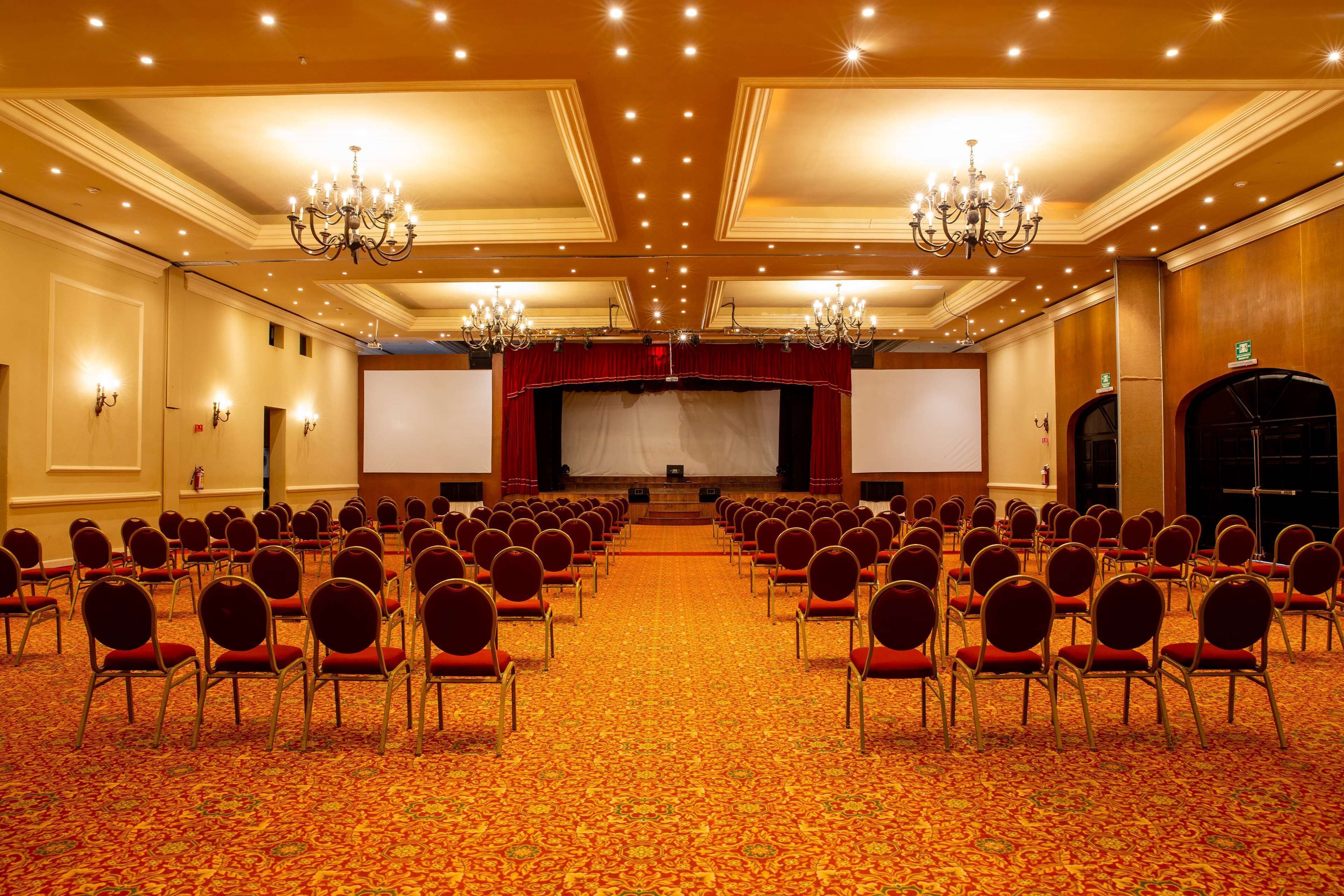 Une salle de conférence avec des rangées de chaises, une scène et un sol recouvert de moquette.