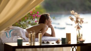 A spa setting with a person lying on a bed, a candle, and a vase with flowers.
