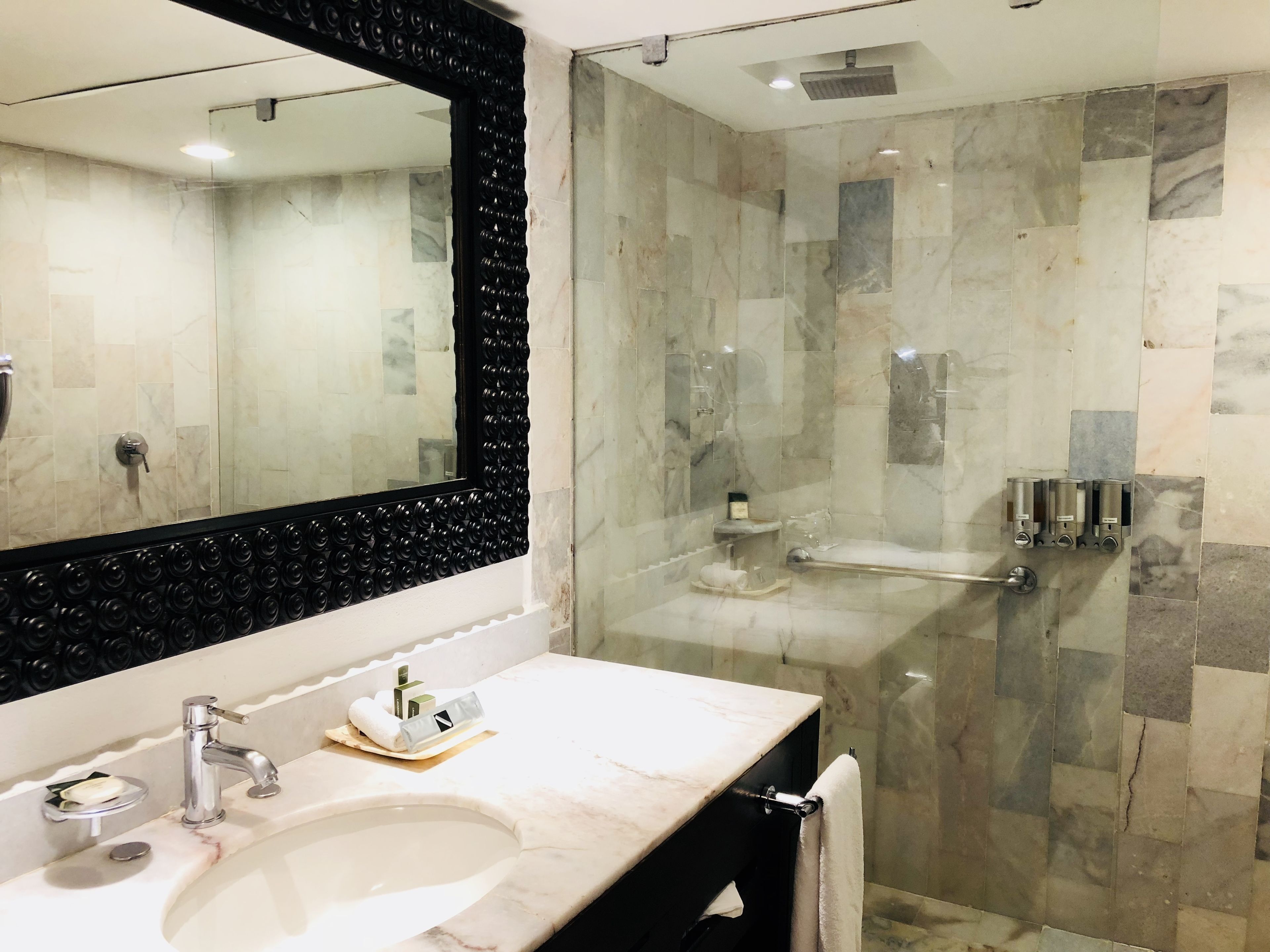 Un baño moderno con un espejo grande, un lavamanos y una ducha con paredes de vidrio.