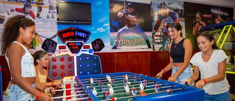A foosball table in a room with a large sports-themed wall, including hockey and baseball imagery.