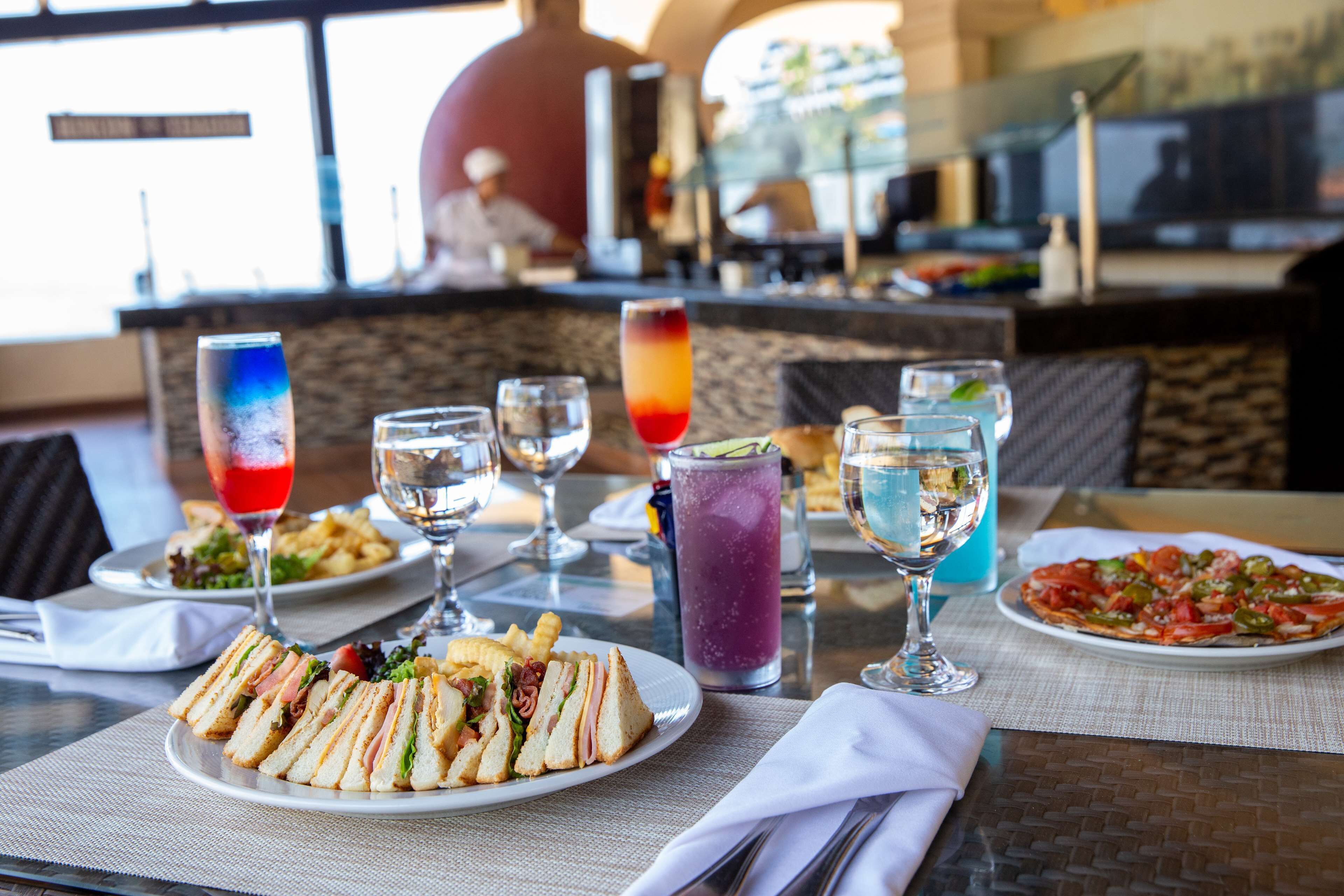 A dining table with a variety of dishes, including a sandwich, a salad, and a pizza, along with several glasses of beverages.