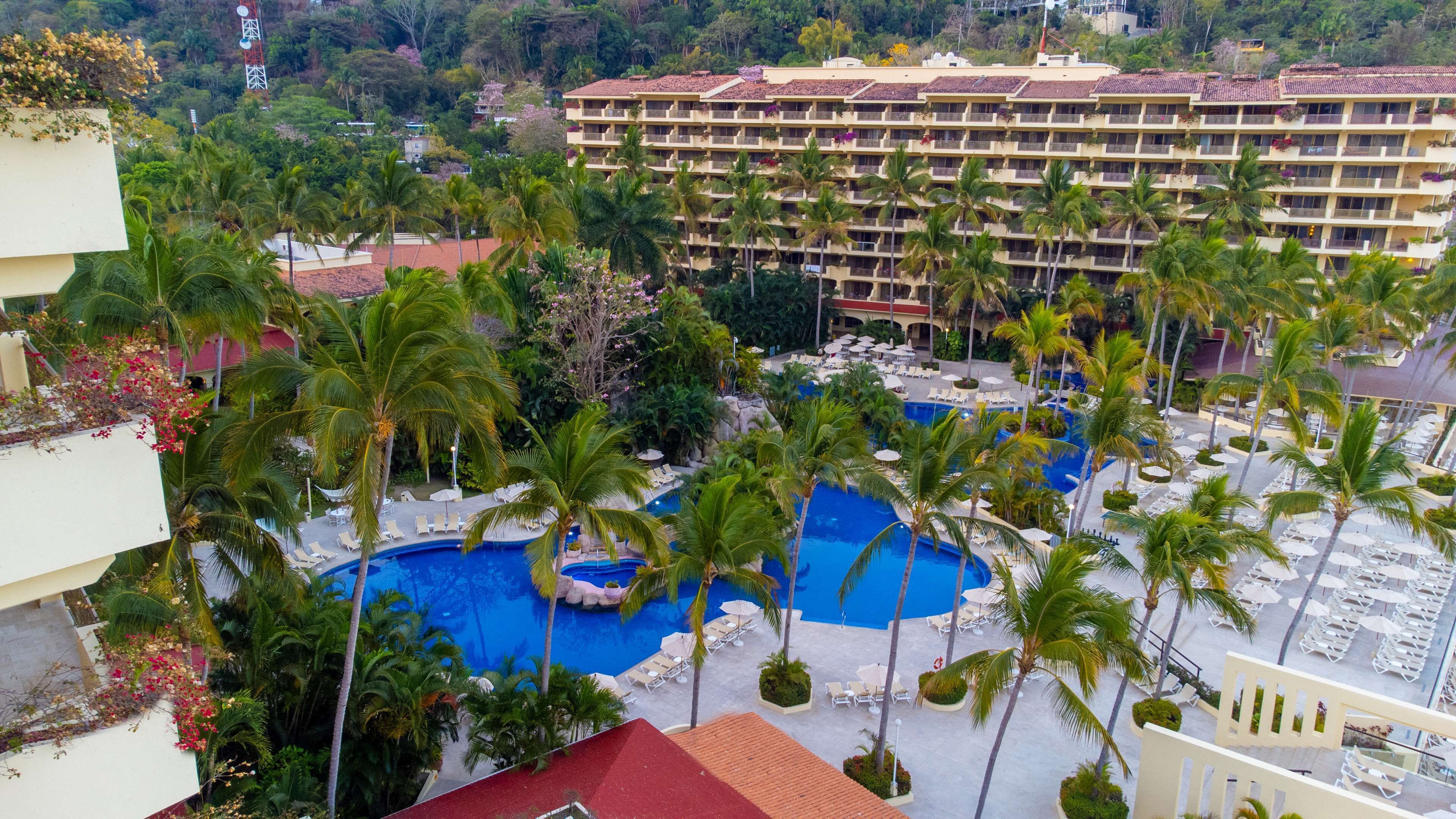 Un hotel con varias piscinas rodeado de palmeras y tumbonas.