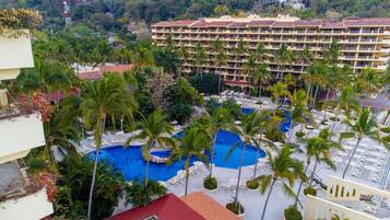 Un hotel con varias piscinas rodeado de palmeras y tumbonas.