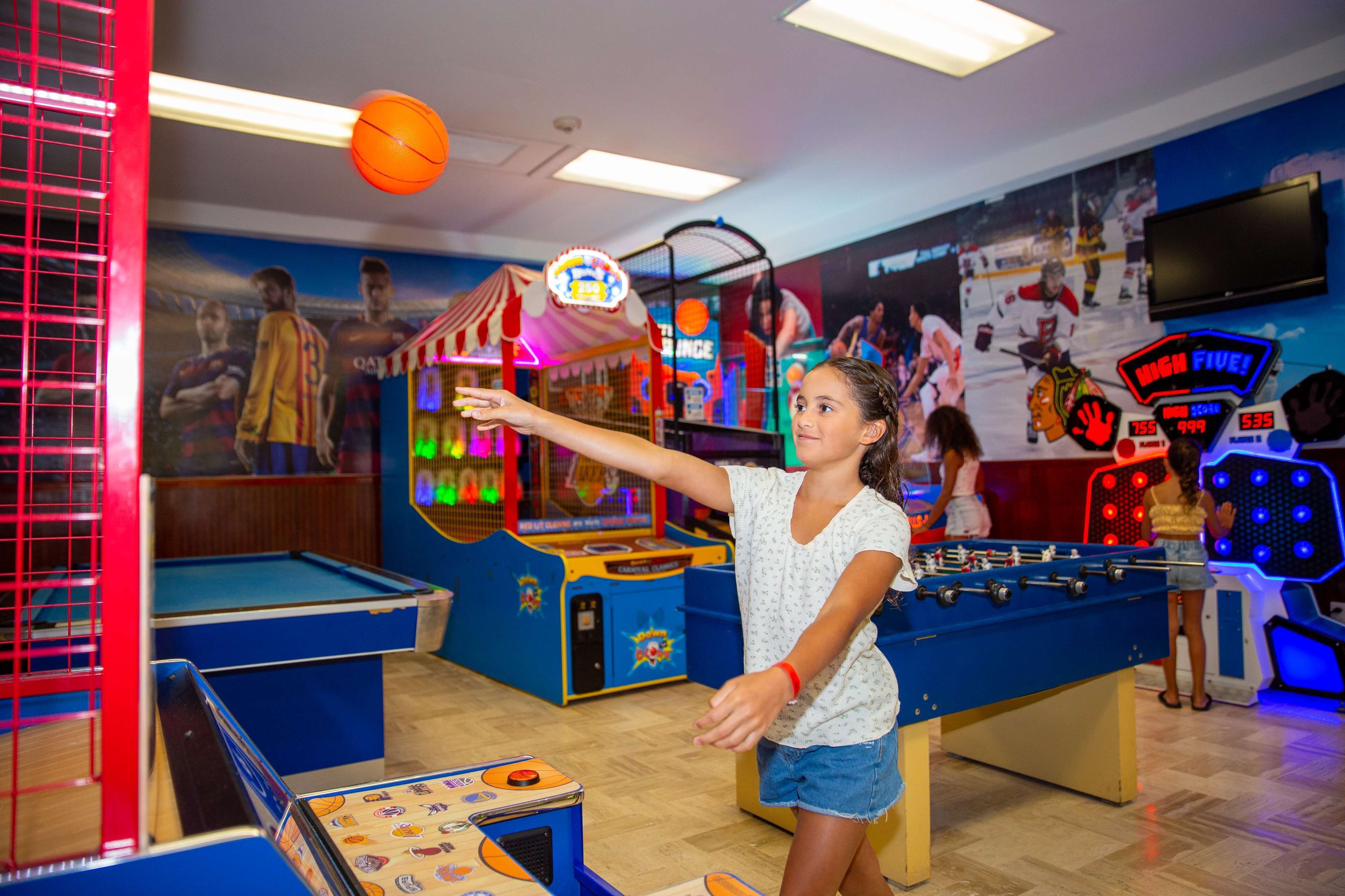 A room with a foosball table, arcade games, and a billiards table.