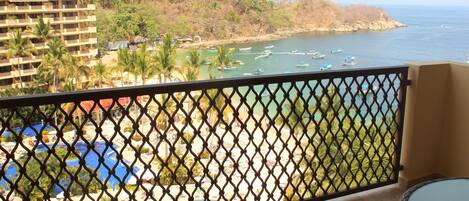 A balcony with a view of a beach, a pool, and a building in the background.
