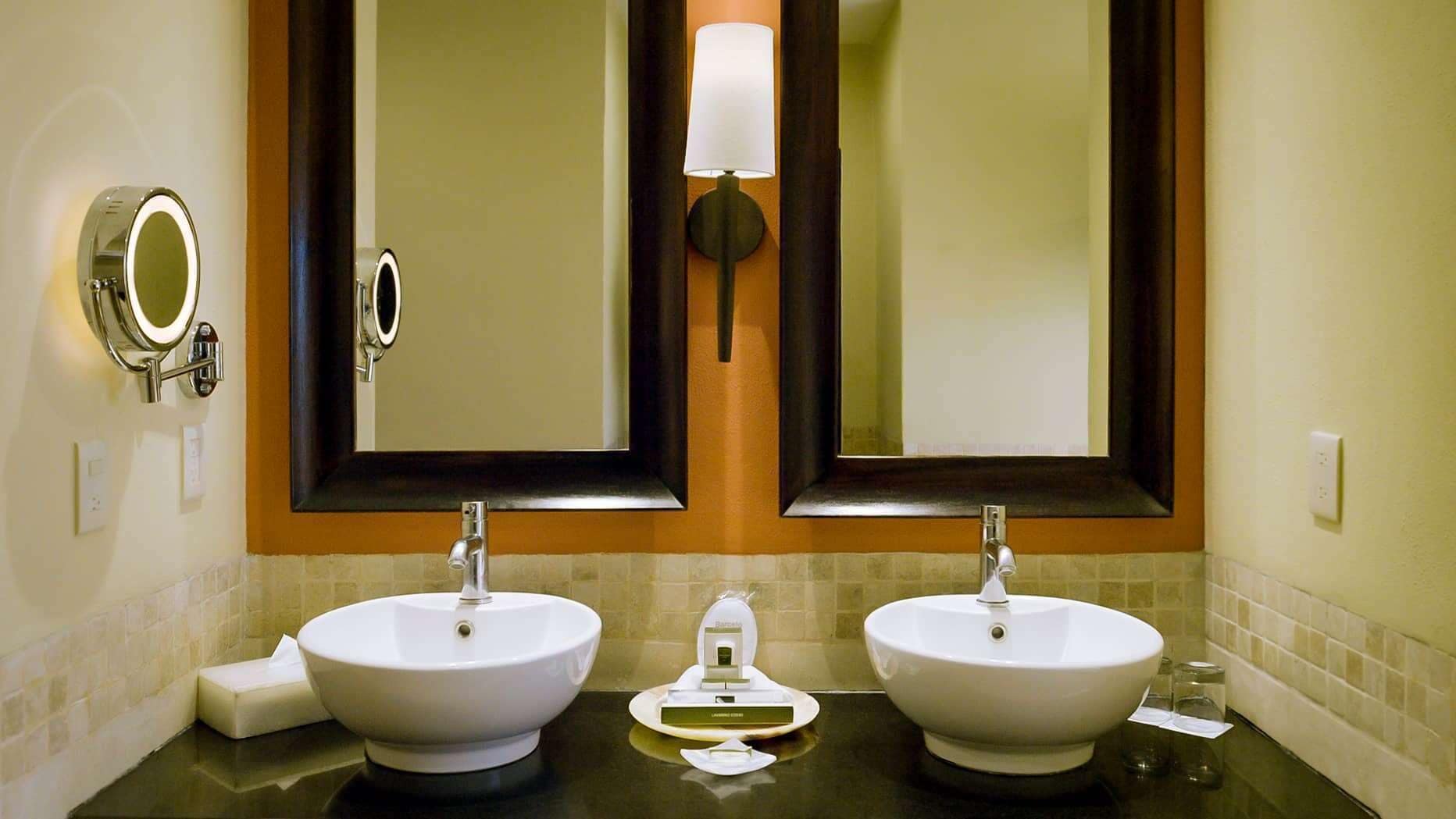 Un bagno con due lavandini, uno specchio e un portalampada a parete.