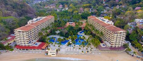 A resort with two large buildings, a central pool, and a beach.