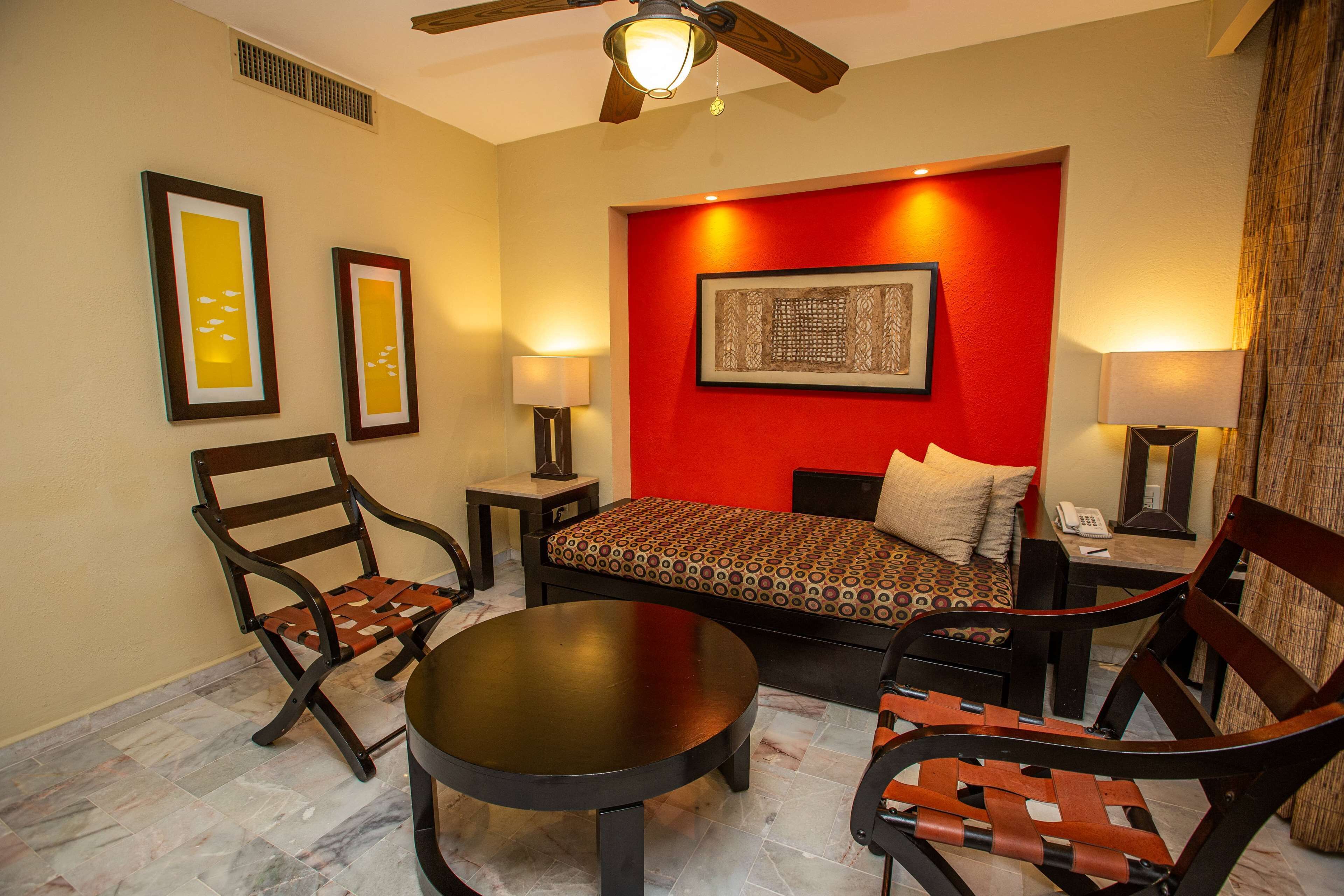 A hotel room with a bed, two chairs, a table, and a ceiling fan.