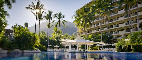 A hotel pool area with palm trees, lounge chairs, and umbrellas.