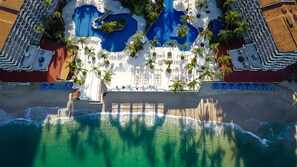 Vista aérea de un resort con varias piscinas, palmeras y acceso a la playa.