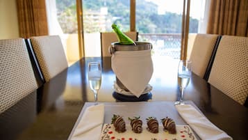 A dining table with a bottle of champagne, two glasses, and a plate of chocolate-covered strawberries.