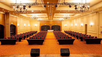 A conference room with rows of chairs, a stage, and chandeliers.