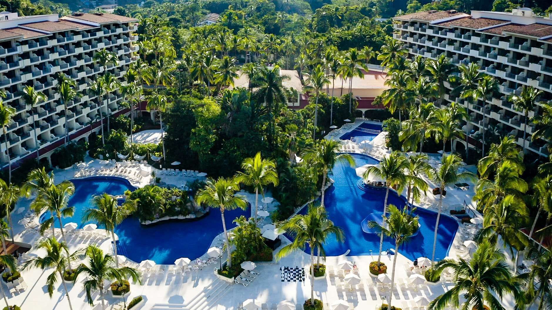 A resort with multiple swimming pools surrounded by palm trees and lounge chairs.