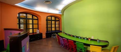A room with a curved green bar, colorful chairs, and arched windows.