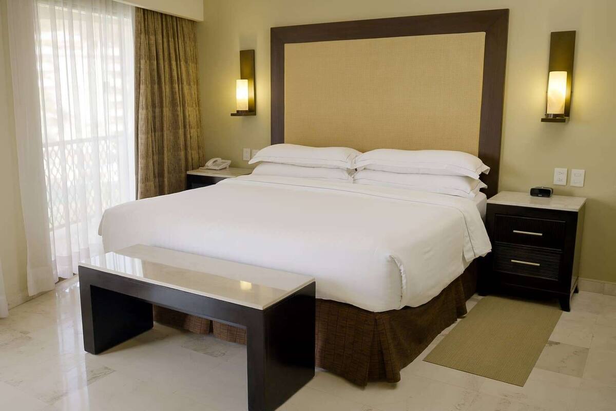 A hotel room with a large bed, bedside tables, a desk, and a window with curtains.