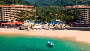 A resort with multiple buildings, a beach, and a pool area surrounded by palm trees.