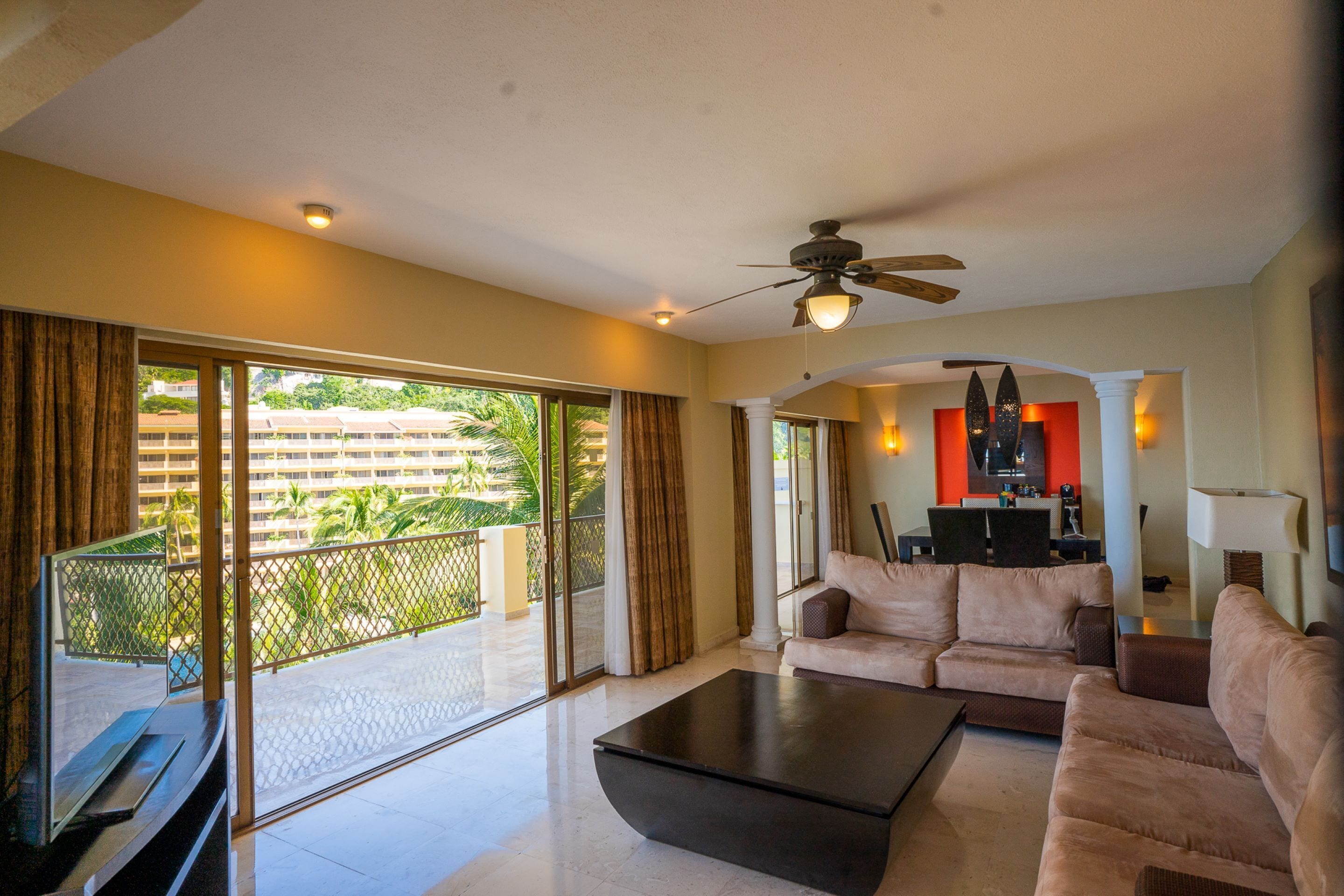 A spacious living room with a large sliding glass door leading to a balcony, a ceiling fan, and a modern coffee table.