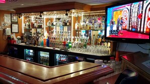 Zona de bar con mostrador, estanterías llenas de botellas de licor y una pantalla de televisión mostrando un partido.