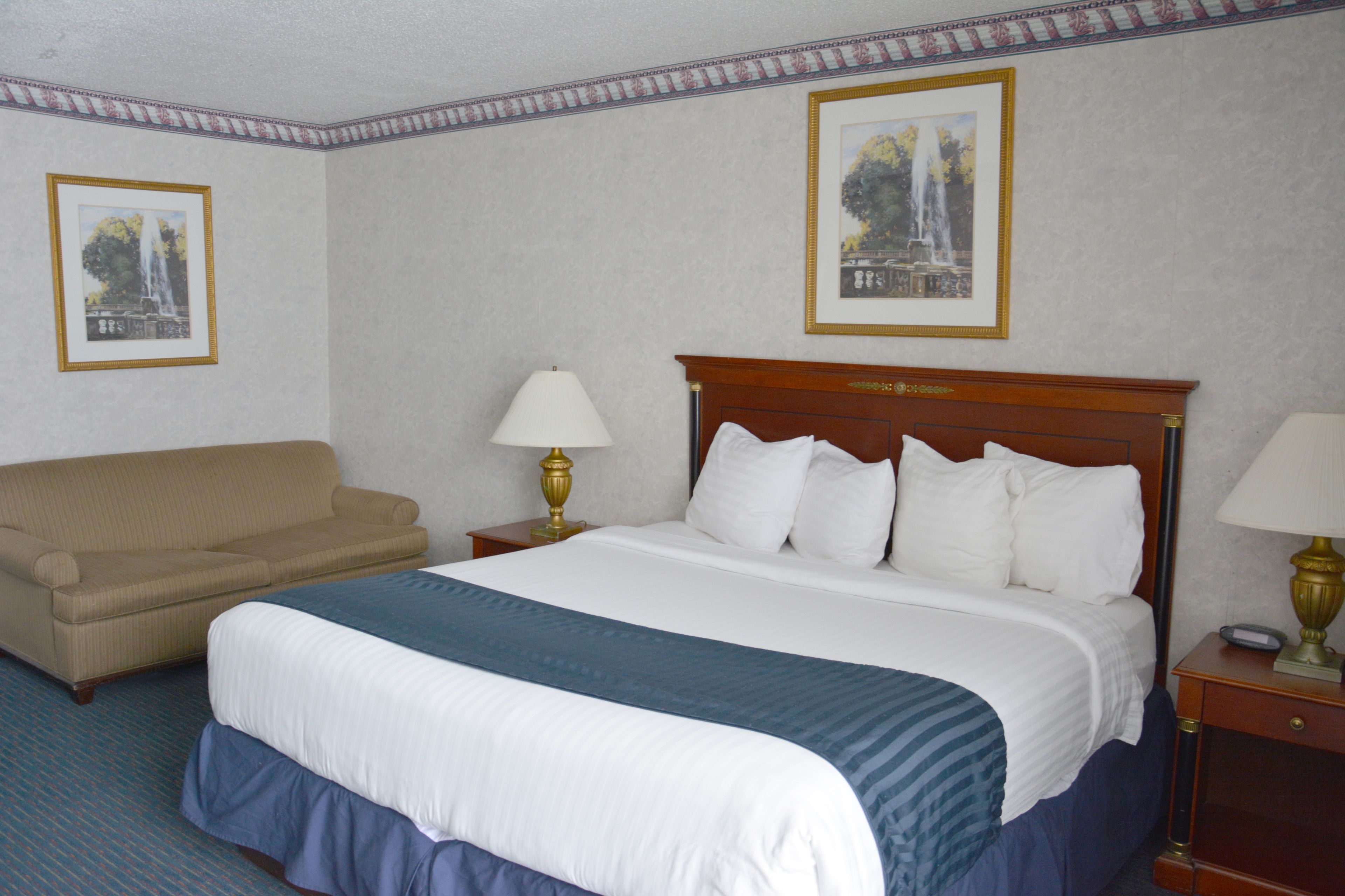 A hotel room with a bed, a sofa, two bedside tables with lamps, and two framed pictures on the walls.