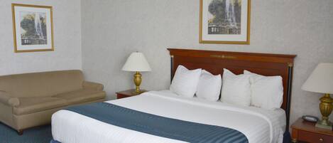 A hotel room with a bed, a sofa, two bedside tables with lamps, and two framed pictures on the walls.