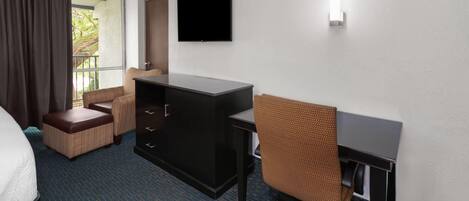 Habitación de hotel con cama, escritorio, silla, cómoda y televisor en la pared.
